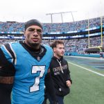 Tre'von Moehrig - Ein Footballspieler in einem blauen Panthers-Trikot mit der Nummer 7 geht mit seinem Helm in der Hand vom Spielfeld, begleitet von einem Mann in einem schwarzen Kapuzenpullover. Das Stadion ist mit Fans gefüllt und im Hintergrund sind Torpfosten zu sehen. Diese Beschreibung wurde mit der FootballR KI automatisch generiert.