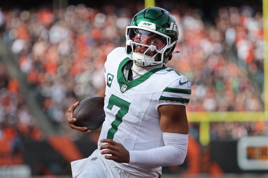 Justin Fields - Ein Football-Spieler in einem weiß-grünen Trikot der New York Jets, mit Helm und der Nummer 7, läuft mit dem Ball auf dem Spielfeld. Die unscharfe Menge und der Torpfosten erinnern an eine schnelle Bewegung während eines Spiels gegen die Cleveland Browns. Diese Beschreibung wurde mit der FootballR KI automatisch generiert.