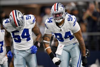 Zwei Footballspieler der Dallas Cowboys in weißen Trikots und silbernen Hosen feiern auf dem Spielfeld. Marshawn Kneeland, der NFL-Talent zeigt, ballt die Faust und schreit, während die verschwommene Menge im Hintergrund brüllt. Diese Beschreibung wurde mit der FootballR KI automatisch generiert.