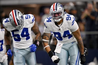 Zwei Footballspieler der Dallas Cowboys in weißen Trikots und silbernen Hosen feiern auf dem Spielfeld. Marshawn Kneeland, der NFL-Talent zeigt, ballt die Faust und schreit, während die verschwommene Menge im Hintergrund brüllt. Diese Beschreibung wurde mit der FootballR KI automatisch generiert.