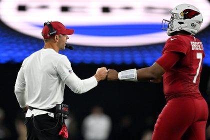 Ein Football-Trainer in einem weißen Hemd und einer roten Mütze gibt dem Cardinals-Spieler Nummer 7, Kyler Murray, in einer roten Arizona Cardinals-Uniform und einem roten Helm, einen Faustschlag. Der Hintergrund ist unscharf mit hellen Stadionlichtern und einem großen Schild über dem Kopf. Diese Beschreibung wurde mit der FootballR KI automatisch generiert.