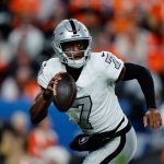 Quarterback Geno Smith - Nummer 7 - der Las Vegas Raiders läuft mit dem Ball in der rechten Hand, den Blick nach vorne gerichtet. Mit seinem silbernen Helm und den schwarzen Handschuhen stürmt er vorwärts, während die orange-blaue Menge im Hintergrund verschwimmt. Diese Beschreibung wurde mit der FootballR KI automatisch generiert.
