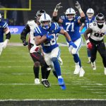 NFL Playoff Picture - Jonathan Taylor in einem blauen Trikot der Indianapolis Colts läuft mit dem Ball, verfolgt von Verteidigern der Atlanta Falcons in Weiß und Schwarz, während eines NFL-Playoff-Spiels. Mannschaftskameraden blockieren auf dem grünen Spielfeld; gelbe Torpfosten und eine unscharfe Menschenmenge füllen den Hintergrund. Diese Beschreibung wurde mit der FootballR KI automatisch generiert.
