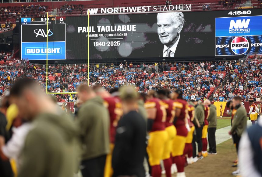 Die Zuschauer im Stadion beobachten, wie die Football-Spieler auf dem Feld stehen. Auf einer großen Leinwand wird eine Hommage an die NFL-Legende und den ehemaligen Commissioner Paul Tagliabue (1940-2025) gezeigt, um sein Vermächtnis während des Spiels zu würdigen. Diese Beschreibung wurde mit der FootballR KI automatisch generiert.