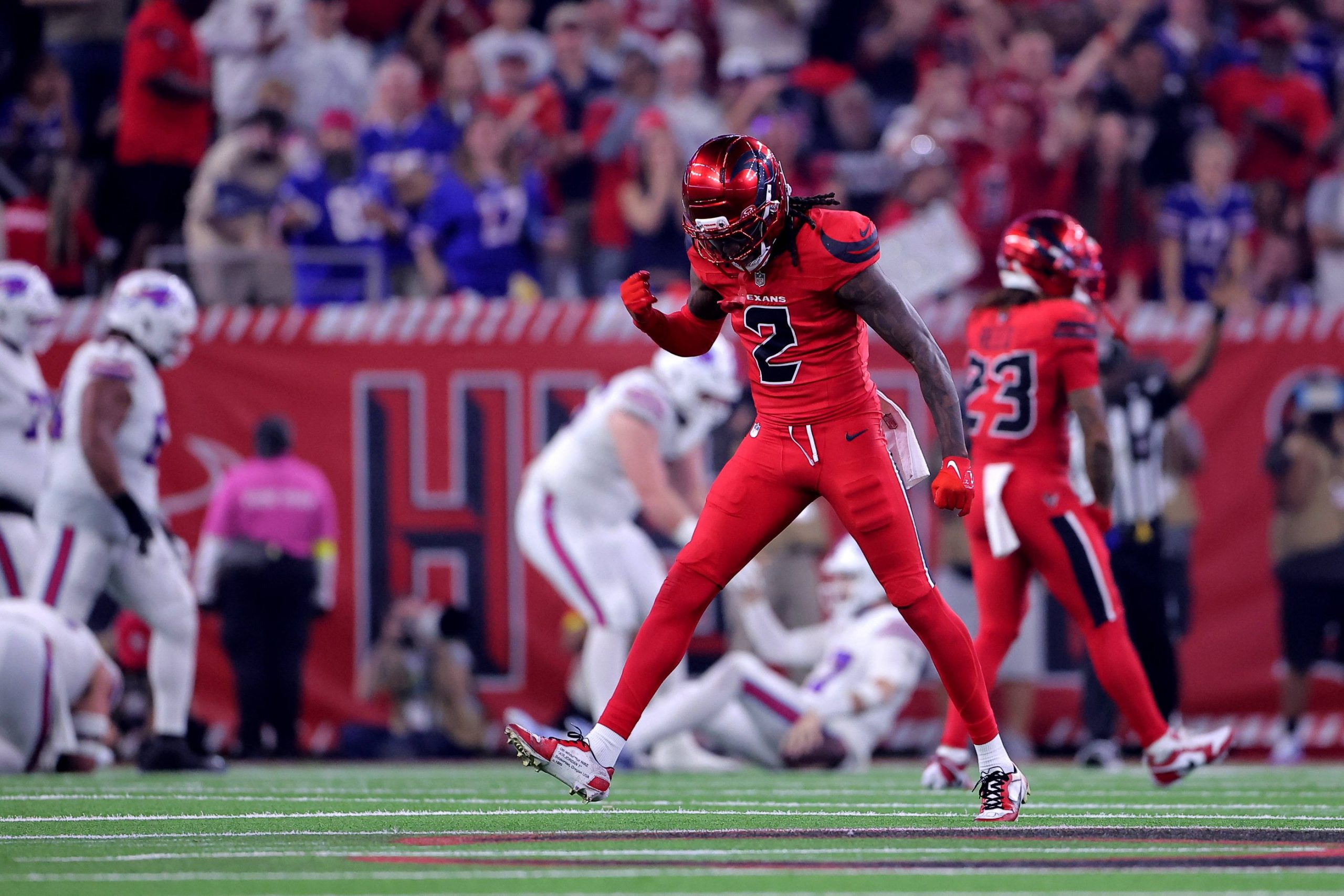 Ein Footballspieler in einem roten Texans-Trikot mit der Nummer 2 ballt die Faust und blickt jubelnd auf das Spielfeld. Im Hintergrund sind andere Spieler und eine jubelnde Menge zu sehen, die Stadionbeleuchtung erhellt die Szene. Diese Beschreibung wurde mit der FootballR KI automatisch generiert.