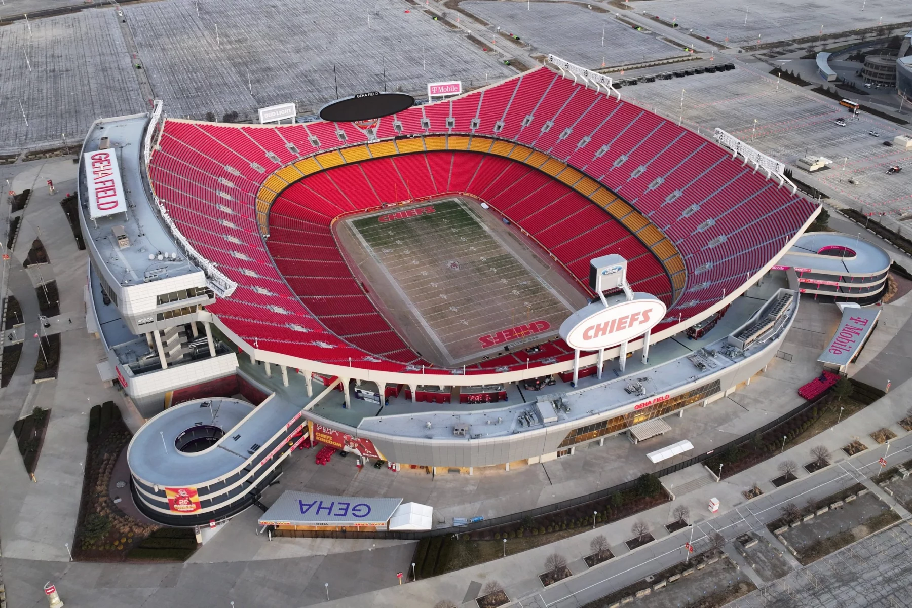 Luftaufnahme des leeren GEHA Field im Arrowhead Stadium, der Heimat der Kansas City Chiefs. Leuchtend rote Sitze umgeben das grüne Football-Feld in Kansas, mit "CHIEFS" in den Endzonen und leeren Parkplätzen rund um das Stadion. Diese Beschreibung wurde mit der FootballR KI automatisch generiert.