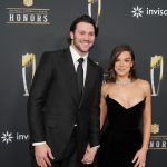 Josh Allen, in schwarzem Anzug und Krawatte, steht lächelnd neben Hailee Steinfeld in einem trägerlosen schwarzen Kleid und einer Diamantenkette auf dem roten Teppich einer NFL Honors Veranstaltung. Sie halten Händchen und posieren für Fotos vor der NFL-Kulisse. Diese Beschreibung wurde mit der FootballR KI automatisch generiert.