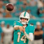 Quinn Ewers - Ein Footballspieler in einem blaugrünen Trikot der Miami Dolphins mit weißem Helm und der Nummer 14 wirft einen Football während eines Spiels. Der Ball befindet sich in der Luft, Tua Tagovailoa und andere Spieler sind im Hintergrund inmitten von jubelnden Zuschauern unscharf zu erkennen. Diese Beschreibung wurde mit der FootballR KI automatisch generiert.