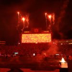 Ein großes Stadion voller Fans bei Nacht. Der Himmel leuchtet rot vom Feuerwerk über einer riesigen hellen Anzeigetafel mit der Aufschrift "Auburn Tigers". Die Stadionbeleuchtung und die Flammen in der Nähe des Spielfelds tragen zu der dramatischen College-Football-Szene bei, und die Tribünen sind mit silhouettierten Zuschauern gefüllt. Diese Beschreibung wurde mit der FootballR KI automatisch generiert.