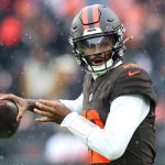Ein Football-Spieler der Browns in Uniform und Helm bereitet sich darauf vor, bei nassem, regnerischem Wetter einen Football zu werfen. Im Hintergrund sind unscharfe Fans zu sehen, die die Intensität und Entschlossenheit der Zukunft der Franchise widerspiegeln. Diese Beschreibung wurde mit der FootballR KI automatisch generiert.