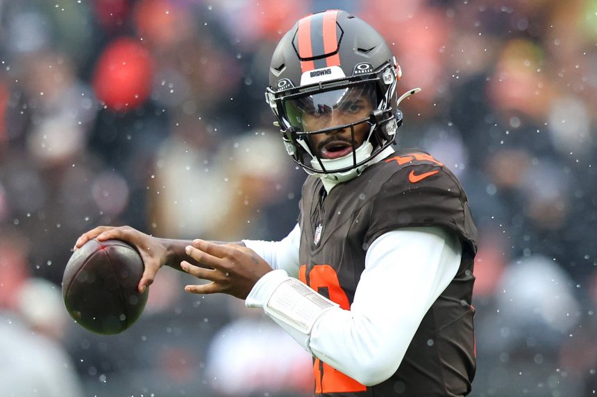 Ein Football-Spieler der Browns in Uniform und Helm bereitet sich darauf vor, bei nassem, regnerischem Wetter einen Football zu werfen. Im Hintergrund sind unscharfe Fans zu sehen, die die Intensität und Entschlossenheit der Zukunft der Franchise widerspiegeln. Diese Beschreibung wurde mit der FootballR KI automatisch generiert.