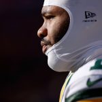 Micah Parsons - Nahaufnahme, Seitenprofil eines Packers-Footballspielers, der einen weißen, gepolsterten Helm und eine grün-gelbe Uniform trägt. Der Spieler blickt konzentriert nach links, wobei helles Sonnenlicht sein Gesicht vor einem dunklen, unscharfen Hintergrund hervorhebt. Diese Beschreibung wurde mit der FootballR KI automatisch generiert.