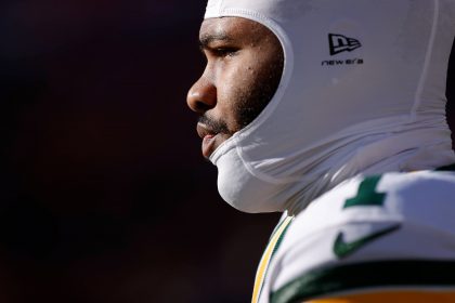 Micah Parsons - Nahaufnahme, Seitenprofil eines Packers-Footballspielers, der einen weißen, gepolsterten Helm und eine grün-gelbe Uniform trägt. Der Spieler blickt konzentriert nach links, wobei helles Sonnenlicht sein Gesicht vor einem dunklen, unscharfen Hintergrund hervorhebt. Diese Beschreibung wurde mit der FootballR KI automatisch generiert.