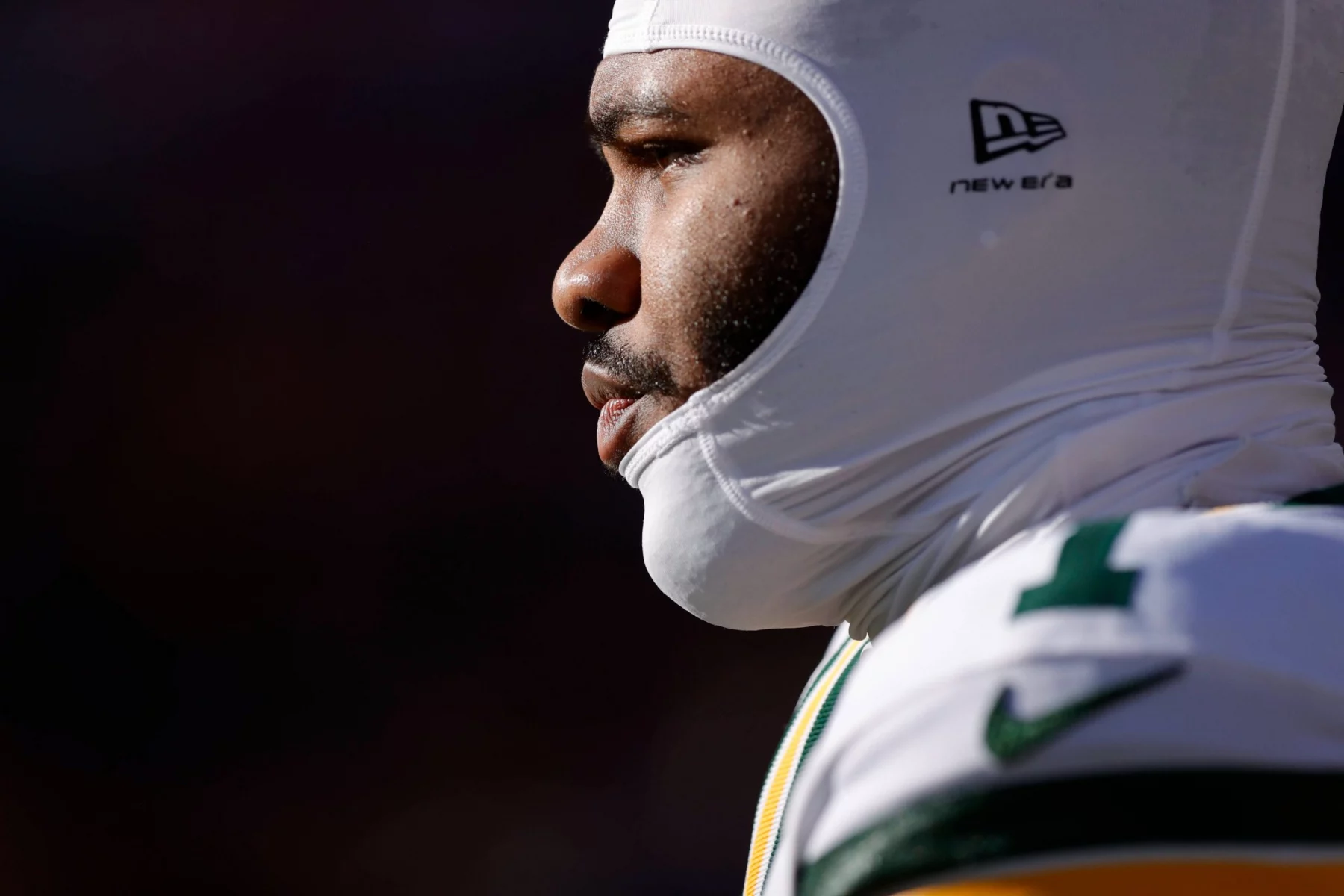 Micah Parsons - Nahaufnahme, Seitenprofil eines Packers-Footballspielers, der einen weißen, gepolsterten Helm und eine grün-gelbe Uniform trägt. Der Spieler blickt konzentriert nach links, wobei helles Sonnenlicht sein Gesicht vor einem dunklen, unscharfen Hintergrund hervorhebt. Diese Beschreibung wurde mit der FootballR KI automatisch generiert.