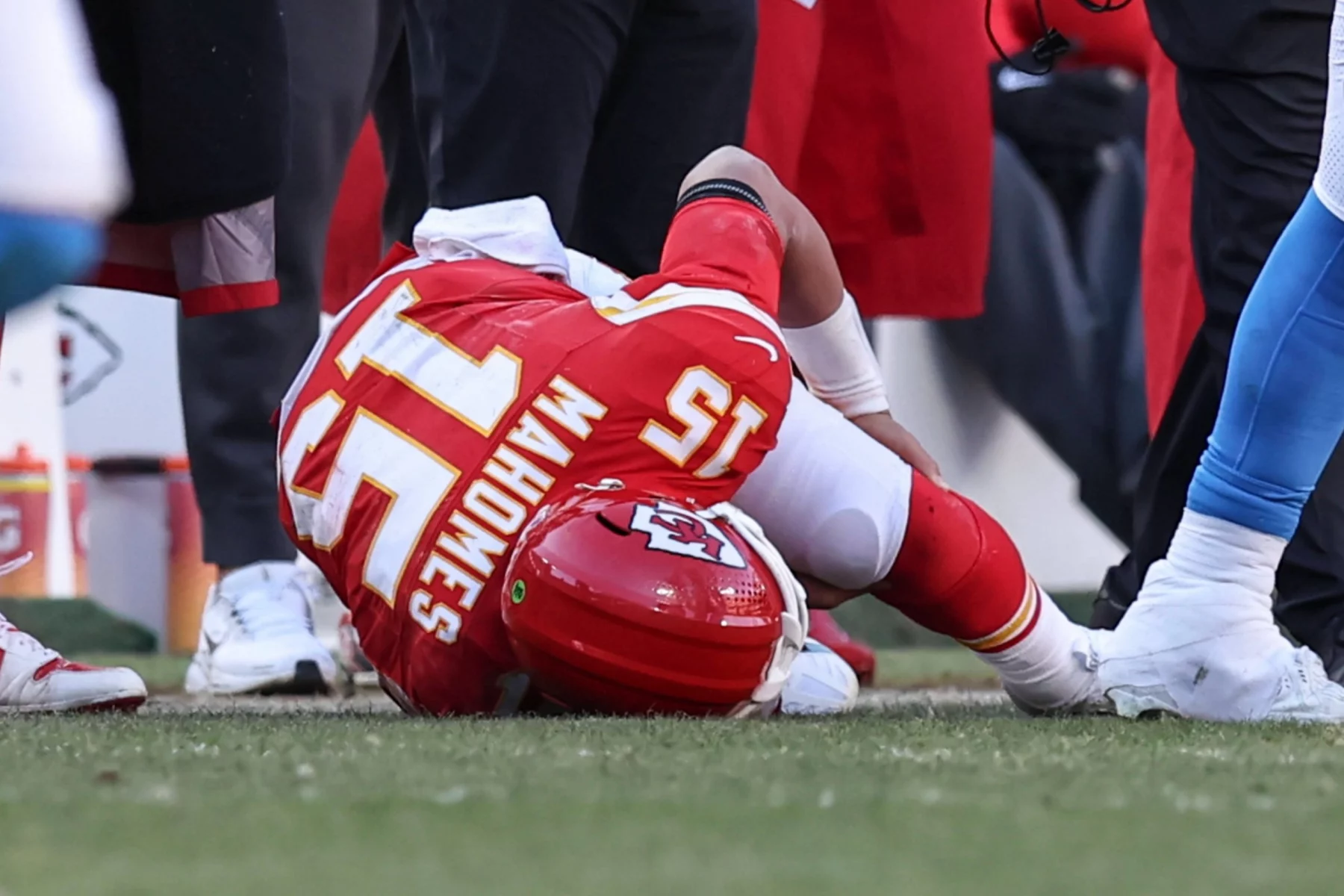 Ein Football-Spieler in einem roten Kansas City Chiefs-Trikot mit der Nummer 15 liegt mit dem Gesicht nach unten, seinen Helm umklammernd, auf dem Feld, umgeben von Spielern und Personal an der Seitenlinie, was auf einen möglichen Kreuzbandriss und eine ungewisse Rückkehr zum Spiel hindeutet. Diese Beschreibung wurde mit der FootballR KI automatisch generiert.
