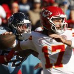 Gardner Minshew - Ein Quarterback der Kansas City Chiefs (#17) bereitet sich darauf vor, einen Football zu werfen, während er einem Verteidiger der Tennessee Titans (#98) während eines NFL-Spiels ausweicht. Der Chiefs-Quarterback trägt einen roten Helm und ein weißes Trikot; der Verteidiger trägt einen dunklen Helm und ein hellblaues Trikot. Diese Beschreibung wurde mit der FootballR KI automatisch generiert.