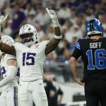 Ein Footballspieler in einem weiß-lila Trikot reißt auf dem Spielfeld feierlich beide Arme hoch. In der Nähe steht Detroit Lions Quarterback Goff mit der Nummer 16 mit dem Rücken zu den Fans, die das Stadion während der intensiven Playoff-Atmosphäre füllen. Diese Beschreibung wurde mit der FootballR KI automatisch generiert.