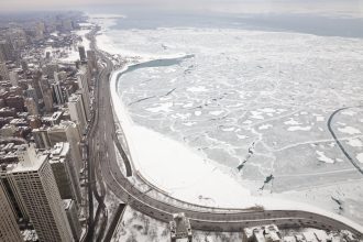 Sean McVay übers Wetter: Luftaufnahme der verschneiten Uferlinie von Chicago-Spiel und eines zugefrorenen Sees mit rissigen Eismustern. Schneebedeckte Straßen schlängeln sich links an Hochhäusern vorbei. Die winterliche, bedeckte Szene strahlt Kälte aus, mit grauem Himmel und wenig Verkehr. Diese Beschreibung wurde mit der FootballR KI automatisch generiert.