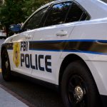 Ein weißes FBI-Polizeiauto parkt auf einer Straße in der Stadt und trägt die Aufschrift "FBI POLICE" und ein Abzeichensymbol. Orangefarbene Verkehrskegel säumen die Straße, während im Hintergrund Bäume und Gebäude zu sehen sind - keine Spur von Schmerzmitteln oder Jim Irsay in der Nähe. Diese Beschreibung wurde mit der FootballR KI automatisch generiert.