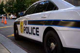 Ein weißes FBI-Polizeiauto parkt auf einer Straße in der Stadt und trägt die Aufschrift "FBI POLICE" und ein Abzeichensymbol. Orangefarbene Verkehrskegel säumen die Straße, während im Hintergrund Bäume und Gebäude zu sehen sind - keine Spur von Schmerzmitteln oder Jim Irsay in der Nähe. Diese Beschreibung wurde mit der FootballR KI automatisch generiert.