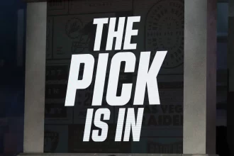 Draft-Picks - In großen, fetten weißen Buchstaben steht auf einem Bildschirm "THE PICK IS IN". Der dunkle Hintergrund und die dramatische Atmosphäre erinnern an die Spannung des NFL Draft 2026, bei dem die Teams auf die Bekanntgabe der Reihenfolge und des Nr.-1-Picks warten. Diese Beschreibung wurde mit der FootballR KI automatisch generiert.