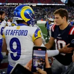 MVP - Ein Rams-Spieler in einem blau-gelben Matthew STAFFORD 9-Trikot schüttelt Drake Maye, der die Nummer 10 der Patriots trägt, auf dem Football-Feld die Hand - ein Moment zwischen den NFL-Award-Finalisten inmitten von Spielern, Medien, Fans und einer Stadionkulisse. Diese Beschreibung wurde mit der FootballR KI automatisch generiert.