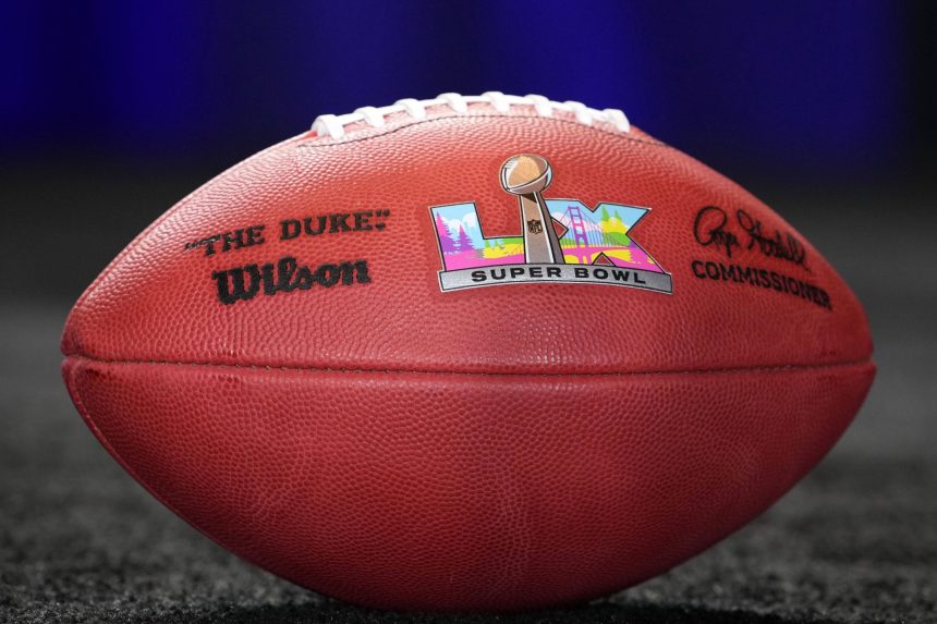 Eine Nahaufnahme eines offiziellen Super Bowl LX Footballs liegt auf einer dunklen, strukturierten Oberfläche. Der Ball zeigt das Super Bowl LX Logo, eine silberne Trophäe, ein farbenfrohes Stadtbild, schwarze Unterschriften, das "The Duke"-Branding von Wilson und eine subtile Anspielung auf die Super Bowl LX-Wertung. Diese Beschreibung wurde mit der FootballR KI automatisch generiert.