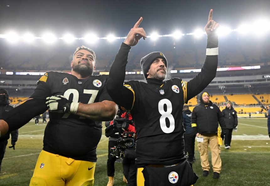 Zwei Footballspieler der Pittsburgh Steelers feiern auf dem Spielfeld in ihren schwarz-gelben Trikots. Der eine streckt den Arm aus, der andere zeigt nach oben und zeigt seinen Stolz auf die AFC North, während im Hintergrund die Sitze und Lichter des Stadions leuchten. Diese Beschreibung wurde mit der FootballR KI automatisch generiert.