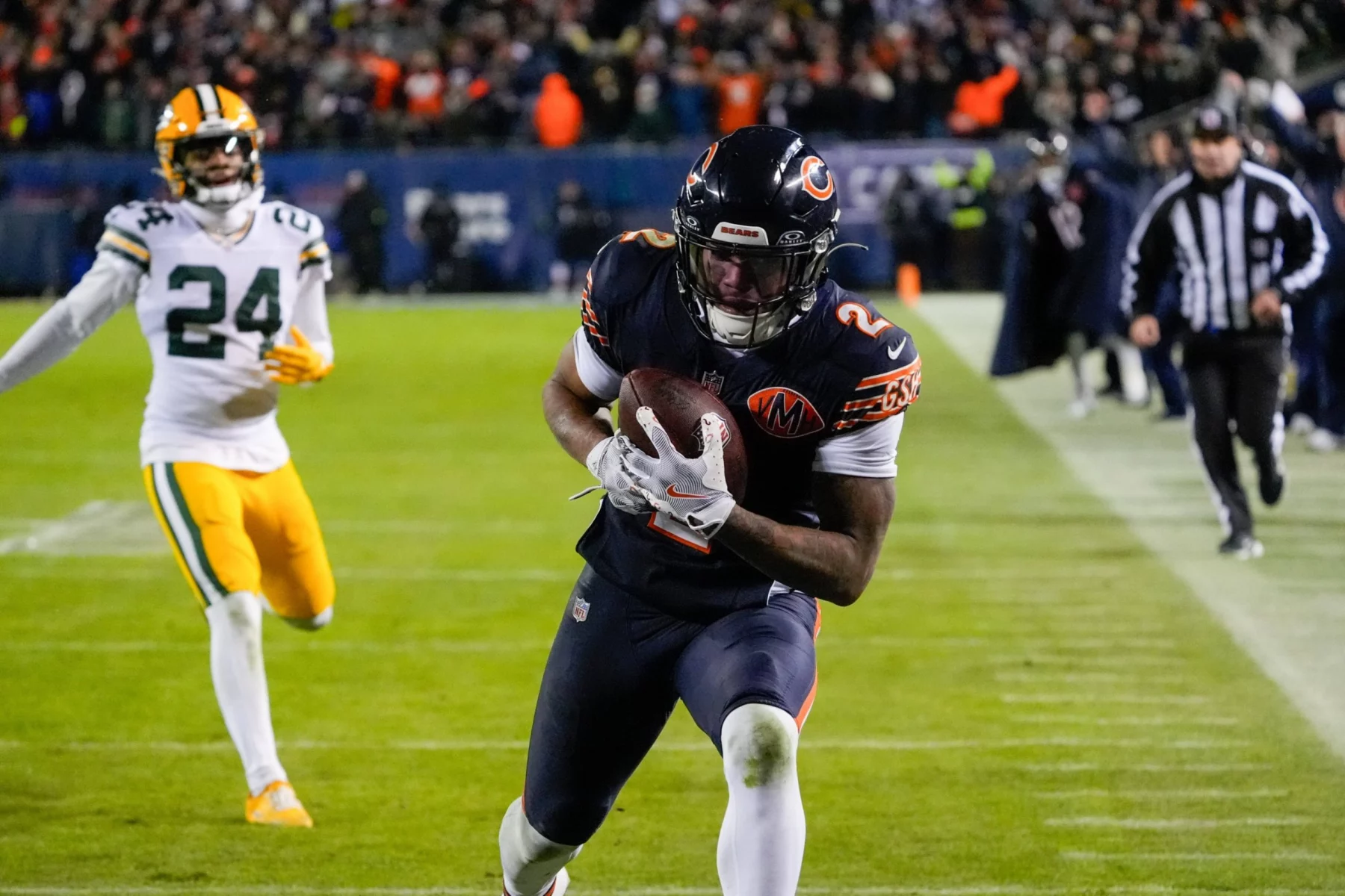 Ein Spieler der Chicago Bears rennt mit einem Football durch die Gegend, während ein Verteidiger der Green Bay Packers ihn während eines hitzigen Divisional-Playoff-Spiels verfolgt. Zuschauer und Schiedsrichter beobachten das Spiel vom Spielfeldrand aus unter hellen Lichtern; das Spiel findet bei Nacht statt. Diese Beschreibung wurde mit der FootballR KI automatisch generiert.