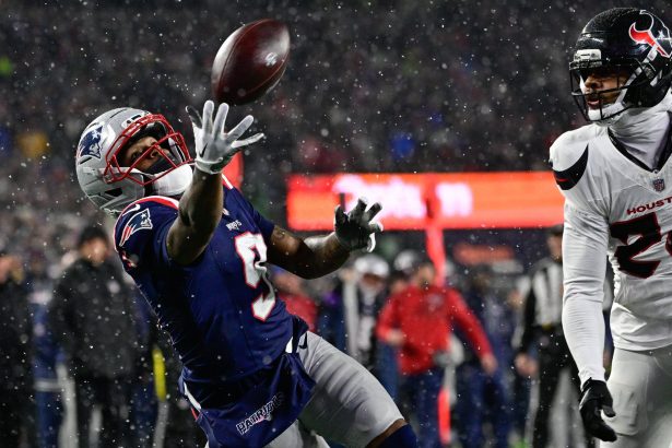 Ein Football-Spieler in einer marineblauen New England Patriots Uniform, möglicherweise Drake Maye, streckt die Hand aus, um einen Ball während eines verschneiten Nachtspiels zu fangen, während ein Texans-Verteidiger in Weiß zusieht. Die Szene ist intensiv, mit Schneefall und verschwommenen Zuschauern im Hintergrund. Diese Beschreibung wurde mit der FootballR KI automatisch generiert.