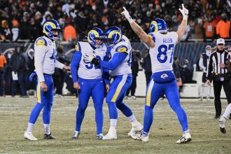 Vier Footballspieler der Los Angeles Rams in blau-weißen Trikots feiern auf einem verschneiten Feld während des NFC Championship Games; einer umarmt den Kicker, während die Nummer 85 (Allen) beide Arme zum Sieg erhebt, während die Zuschauer von der Tribüne aus zusehen. Diese Beschreibung wurde mit der FootballR KI automatisch generiert.