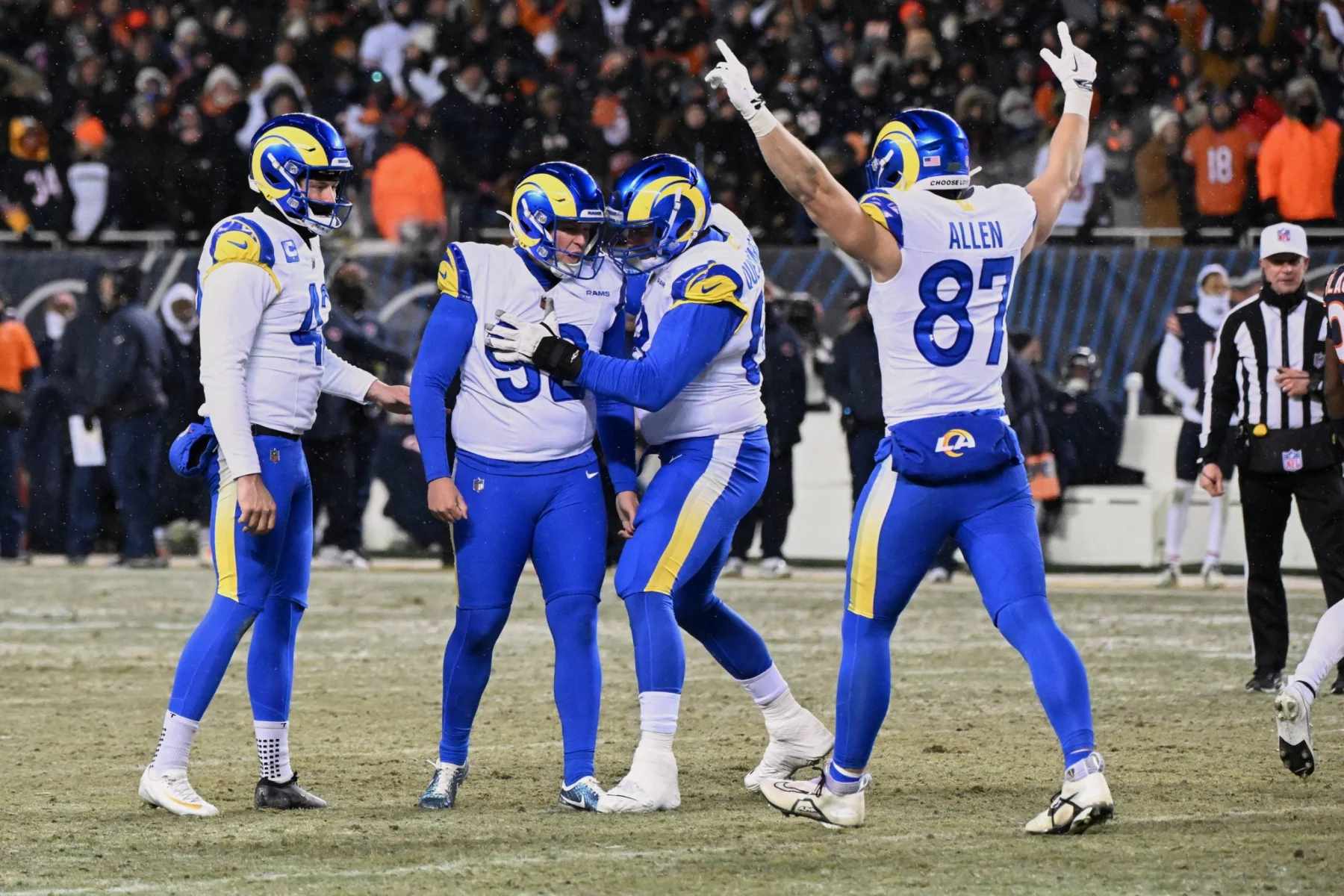 Vier Footballspieler der Los Angeles Rams in blau-weißen Trikots feiern auf einem verschneiten Feld während des NFC Championship Games; einer umarmt den Kicker, während die Nummer 85 (Allen) beide Arme zum Sieg erhebt, während die Zuschauer von der Tribüne aus zusehen. Diese Beschreibung wurde mit der FootballR KI automatisch generiert.