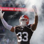 Browns Safety Ronnie Hickman, in voller Uniform, steht mit erhobenen Armen inmitten von Rauch auf einem Stadionfeld, mit Fans im Hintergrund. Alt-Text wurde KI-generiert.