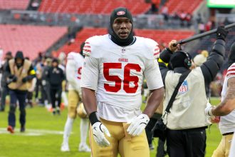 Keion White - Ein Footballspieler, der ein weiß-rotes 49ers-Trikot mit der Nummer 56 trägt, steht nach einem Spiel auf dem Feld und erinnert an Keion Whites entschlossenes Auftreten. Alt-Text wurde KI-generiert.