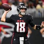 Ein Football-Spieler im Trikot der Atlanta Falcons mit der Nummer 18 bereitet sich darauf vor, während eines Spiels einen Football zu werfen, was die dynamische Energie des Teams auch nach der Verpflichtung von Kirk Cousins unterstreicht. Alt-Text wurde KI-generiert.