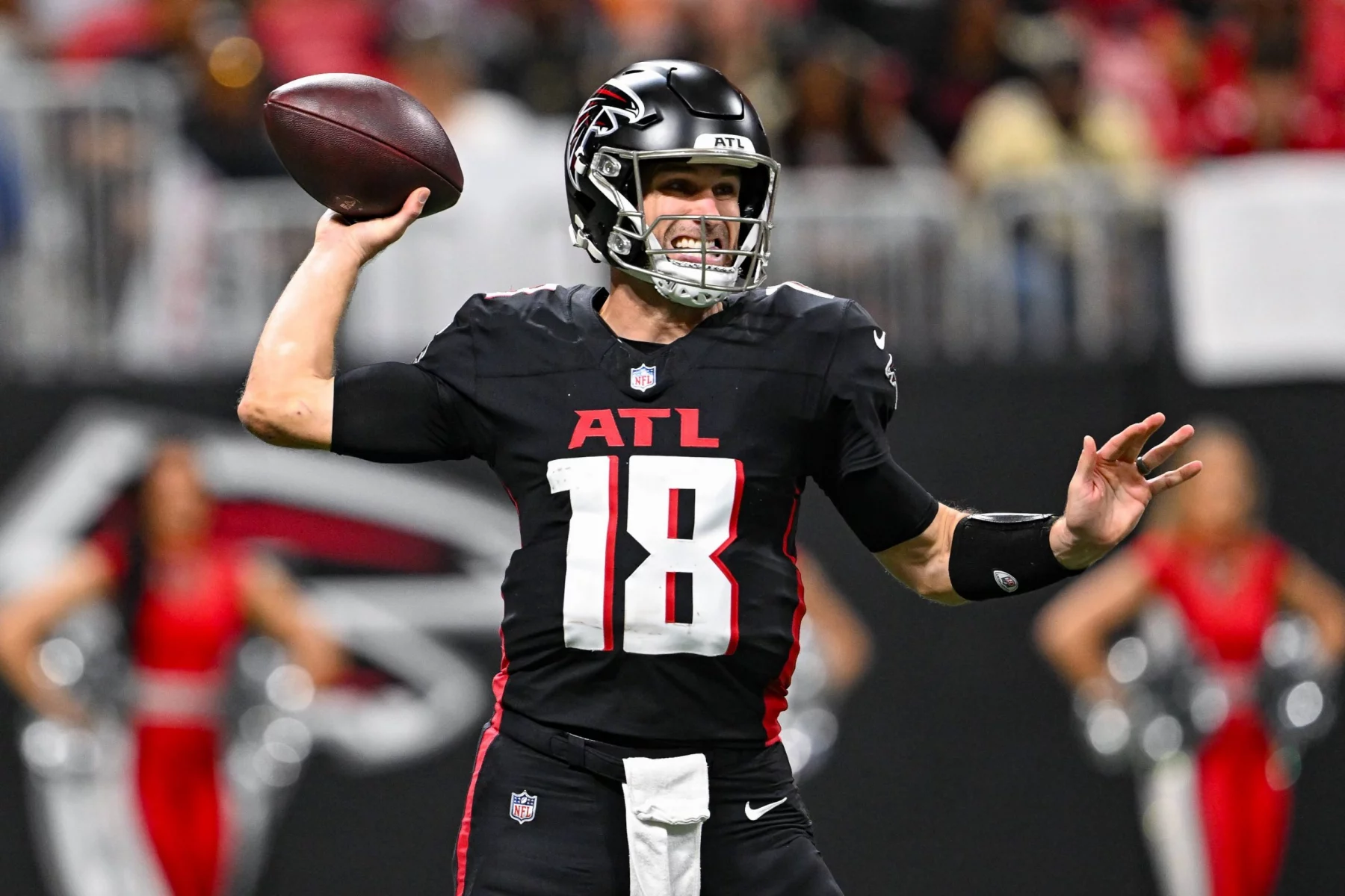 Ein Football-Spieler im Trikot der Atlanta Falcons mit der Nummer 18 bereitet sich darauf vor, während eines Spiels einen Football zu werfen, was die dynamische Energie des Teams auch nach der Verpflichtung von Kirk Cousins unterstreicht. Alt-Text wurde KI-generiert.