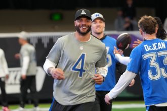 Pro Bowl Games 2026 - Dak Prescott, der ein graues NFL-Shirt mit der Nummer 4 trägt, lächelt, während er mit anderen Spielern in blauen und grauen Trikots an einem NFC vs. AFC Flag Football-Event teilnimmt. Alt-Text wurde KI-generiert.