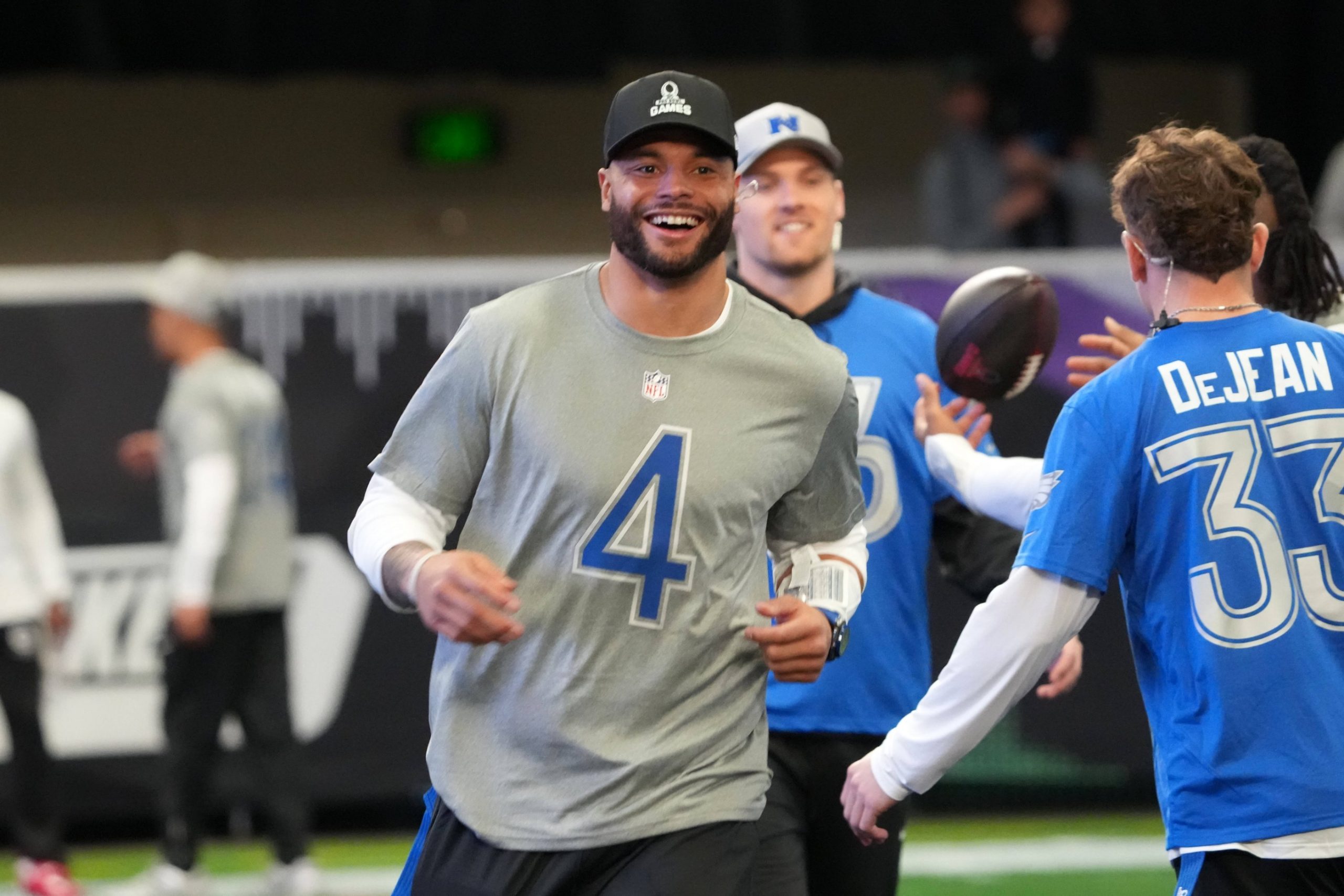 Pro Bowl Games 2026 - Dak Prescott, der ein graues NFL-Shirt mit der Nummer 4 trägt, lächelt, während er mit anderen Spielern in blauen und grauen Trikots an einem NFC vs. AFC Flag Football-Event teilnimmt. Alt-Text wurde KI-generiert.