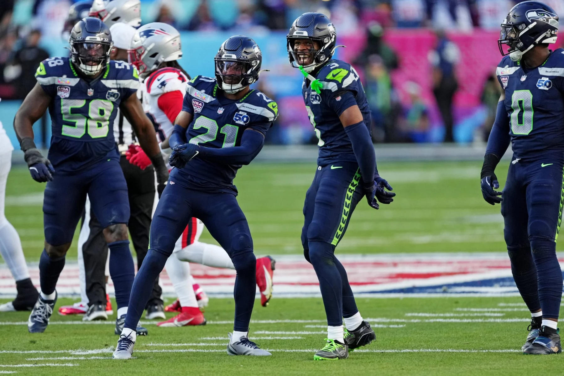 Super Bowl LX - Die Spieler der Seattle Seahawks feiern während eines Footballspiels auf dem Spielfeld und zeigen ihre starke Verteidigung, während im Hintergrund Spieler der New England Patriots zu sehen sind. Alt-Text wurde KI-generiert.