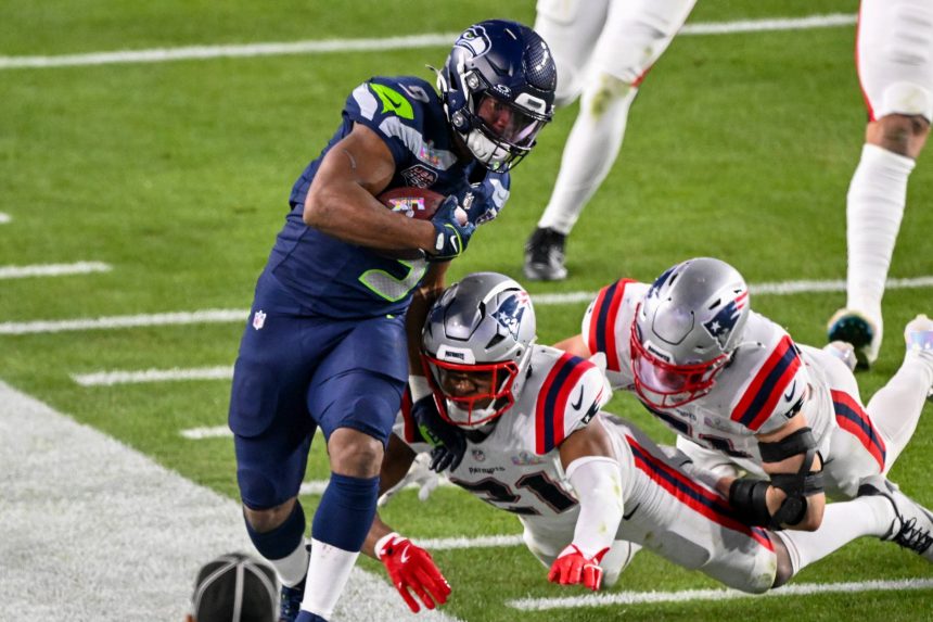 Kenneth Walker III von den Seattle Seahawks rennt mit dem Football, während zwei Verteidiger der New England Patriots versuchen, ihn während eines NFL-Spiels zu tackeln. Dabei zeigt er Fähigkeiten, die eines Super Bowl LX MVP-Anwärters würdig sind. Alt-Text wurde KI-generiert.