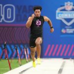 Kenyon Sadiq - Ein Athlet in einem schwarzen Outfit mit der Aufschrift "23 TE" absolviert beim NFL Scouting Combine 2026 einen 40-Yard-Lauf, umgeben von Zeitmessgeräten auf einem Hallenfeld neben anderen herausragenden Tight Ends und Defensive Backs. Alt-Text wurde KI-generiert.