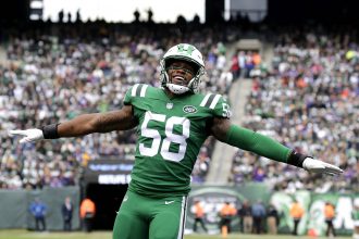 Darron Lee, Linebacker der New York Jets, trägt die Nummer 58 und steht während eines Spiels mit ausgestreckten Armen auf dem Spielfeld. Alt-Text wurde KI-generiert.