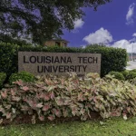 Stein mit Aufschrift Louisiana Tech University umgeben von bunten Pflanzen und grünen Büschen bei blauem Himmel