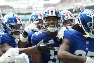 Eine Gruppe von New York Giants-Footballspielern, darunter Bobby Okereke in ihren charakteristischen blauen Trikots, feiert während eines Spiels gemeinsam auf dem Spielfeld. Alt-Text wurde KI-generiert.