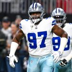 Der Dallas Cowboys-Footballspieler Osa Odighizuwa, der die Trikotnummer 97 trägt, steht während eines Spiels auf dem Spielfeld, während ein anderer Spieler und Zuschauer im Hintergrund zu sehen sind. Alt-Text wurde KI-generiert.
