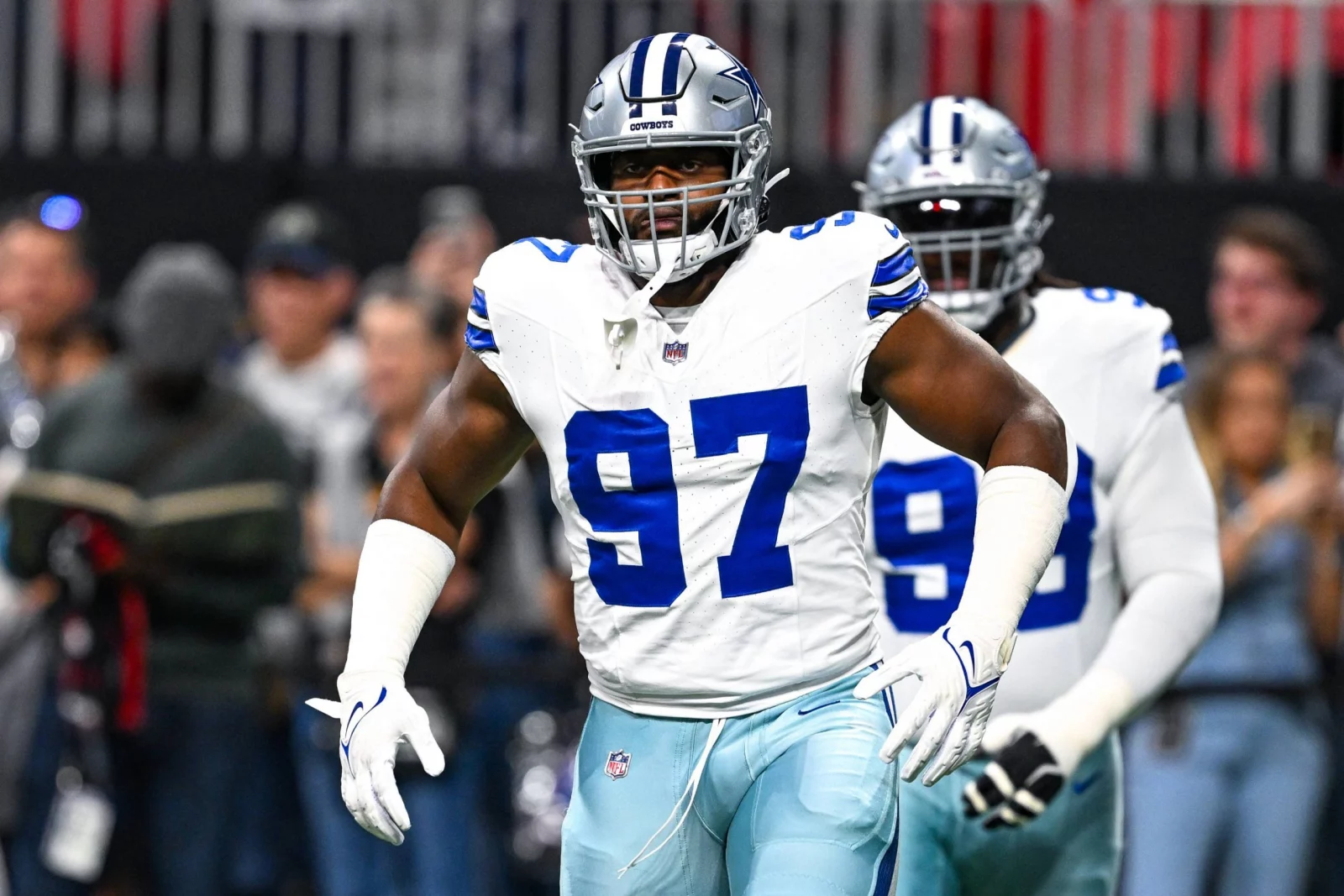 Der Dallas Cowboys-Footballspieler Osa Odighizuwa, der die Trikotnummer 97 trägt, steht während eines Spiels auf dem Spielfeld, während ein anderer Spieler und Zuschauer im Hintergrund zu sehen sind. Alt-Text wurde KI-generiert.