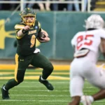 Quarterback Cole Payton in einem grün-gelben Trikot läuft mit dem Ball und zeigt dabei auf einen Verteidiger in einem weiß-roten Trikot - und zeigt damit Fähigkeiten, die beim NFL Draft 2026 zum Tragen kommen könnten. Alt-Text wurde KI-generiert.