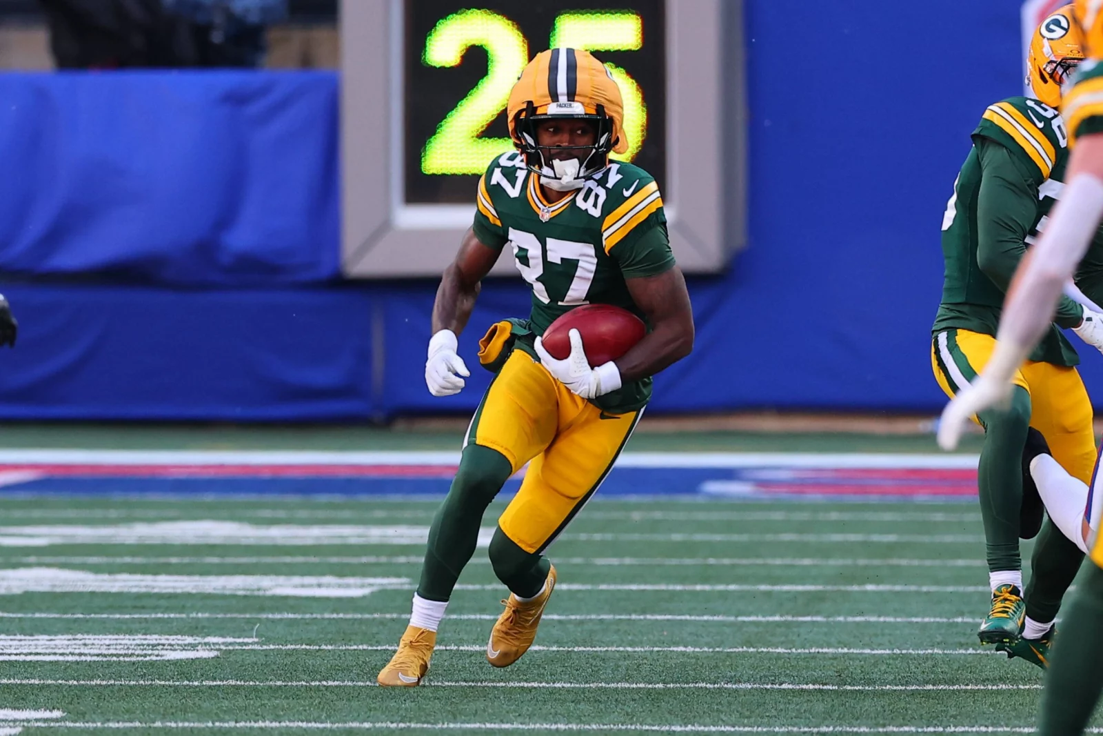 Der Wide Receiver der Packers, Romeo Doubs, läuft während eines Spiels in der grün-gelben Uniform des Teams mit dem Ball. Alt-Text wurde KI-generiert.