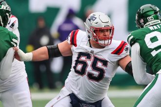 Ein Offensive Lineman der Patriots in einem weißen Trikot blockt einen Verteidiger der New York Jets während eines Footballspiels und zeigt dabei Fähigkeiten, die an Garrett Bradbury erinnern. Alt-Text wurde KI-generiert.