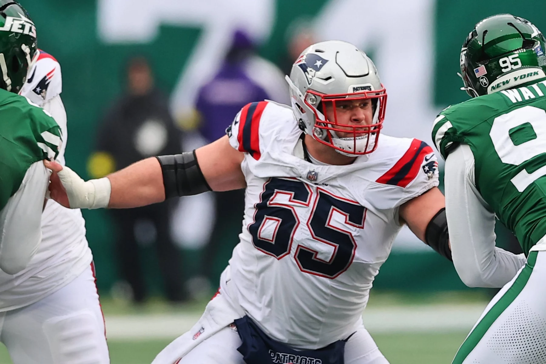 Ein Offensive Lineman der Patriots in einem weißen Trikot blockt einen Verteidiger der New York Jets während eines Footballspiels und zeigt dabei Fähigkeiten, die an Garrett Bradbury erinnern. Alt-Text wurde KI-generiert.
